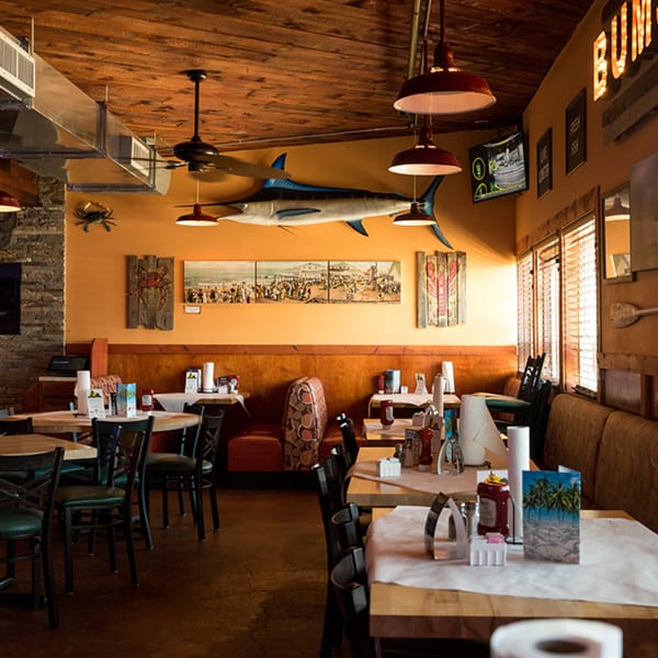 Interior of Bum Rogers Crab House with nautical decor, wooden tables, and orange booth seating.