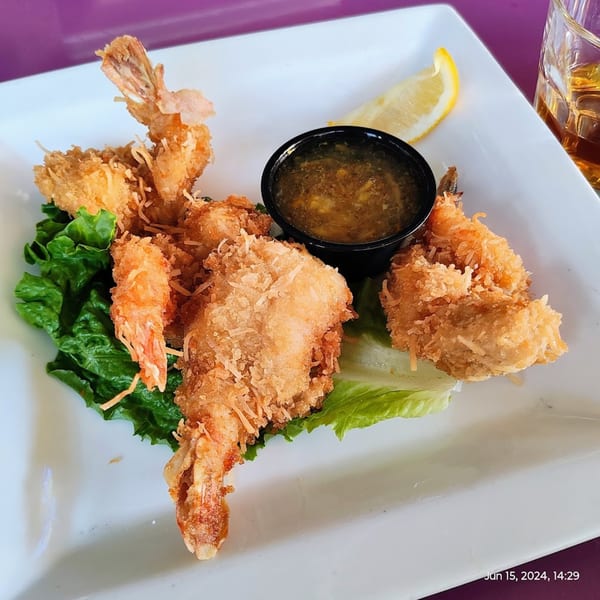 Coconut shrimp with dipping sauce, lettuce, and a lemon wedge on a white plate.