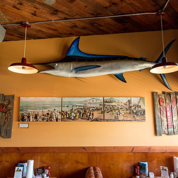 A mounted marlin, vintage beach scene triptych, and lobster art adorn the crab house wall.