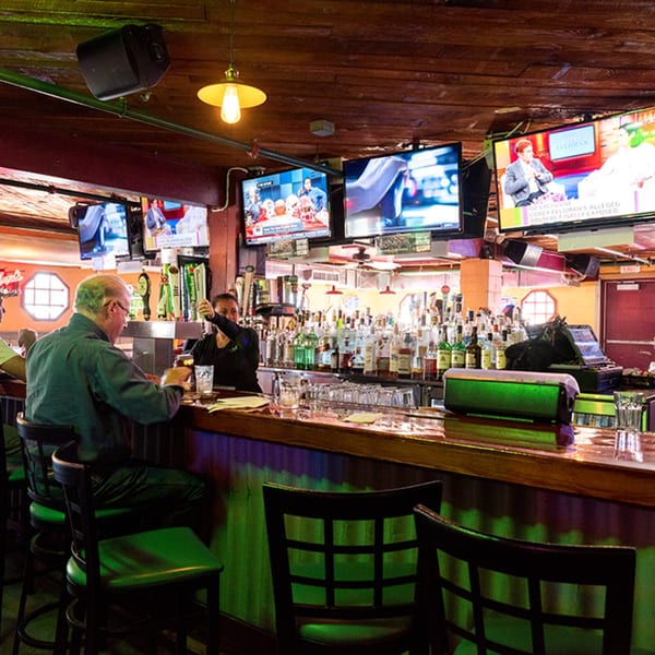 A bartender serves a customer at the Bum Rogers Crab House & Tavern bar, with multiple TVs overhead.