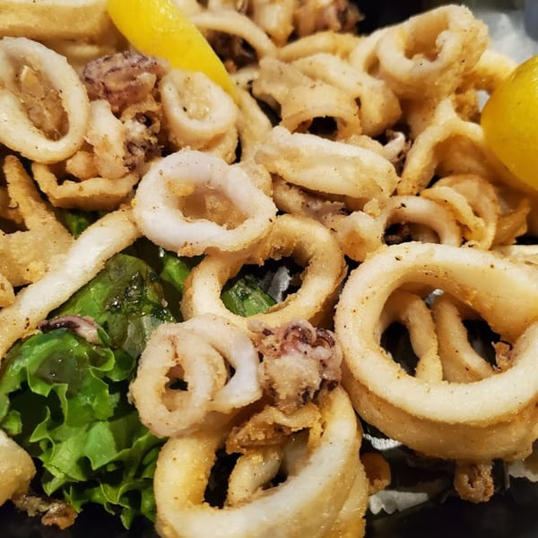 Close-up of crispy fried calamari rings with lemon wedges and green lettuce at Bum Rogers Crab House.