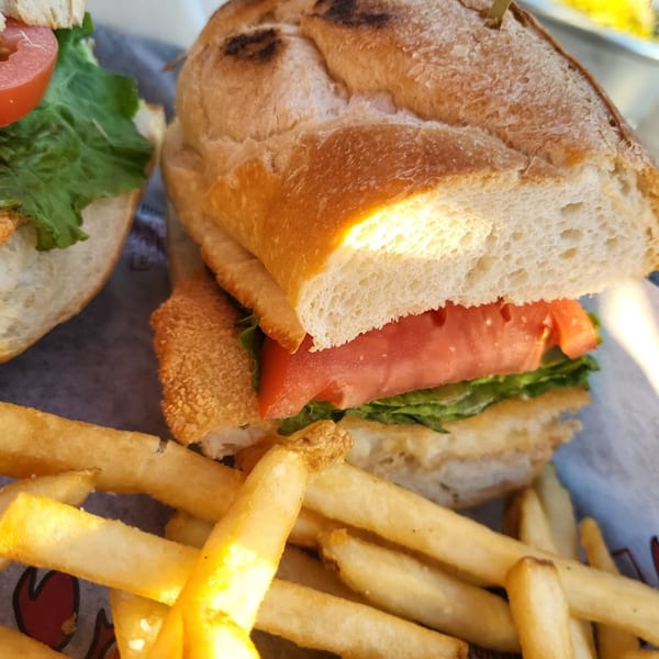 A fried fish sandwich with lettuce and tomato, served with a side of golden french fries.